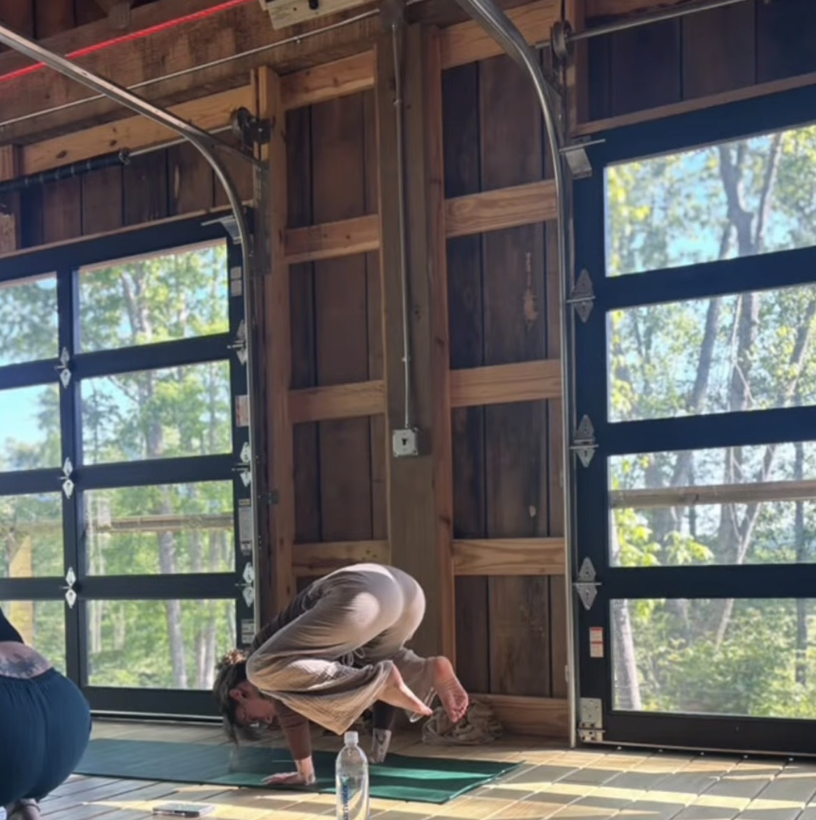 A woman in crow pose framed by sunlit barn doors